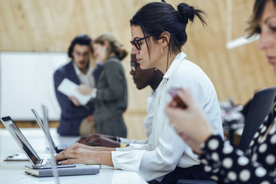 Businesswoman using laptop while sitting amidst colleagues in coworking office