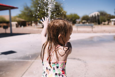 Playful girl playing with water in park during summer