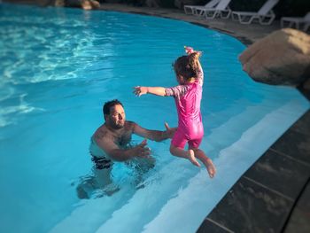 Full length of daughter jumping towards father in swimming pool