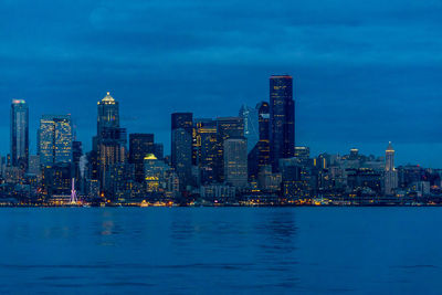 Illuminated buildings by sea against sky at dusk