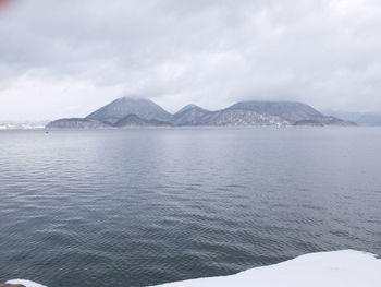 Scenic view of sea by snowcapped mountains against sky