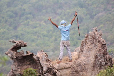 Rear view of man standing with arms outstretched on rock