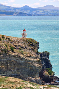 Lighthouse on rock by sea against mountain