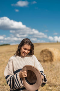 Smiling young woman holding camera on field against sky