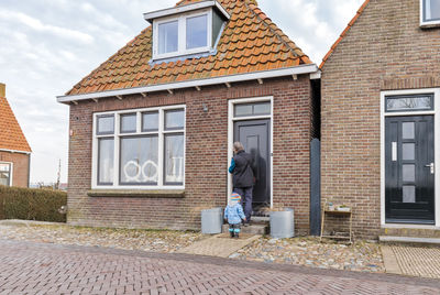 Rear view full length of man with granddaughter standing outside house