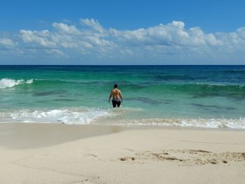 Rear view of man standing at beach against sky