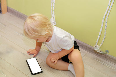 A small child sits on the floor and looks at a mobile phone. a kid with white hair looks at a mobile