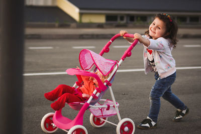 Cute girl with doll in baby stroller walking on roads