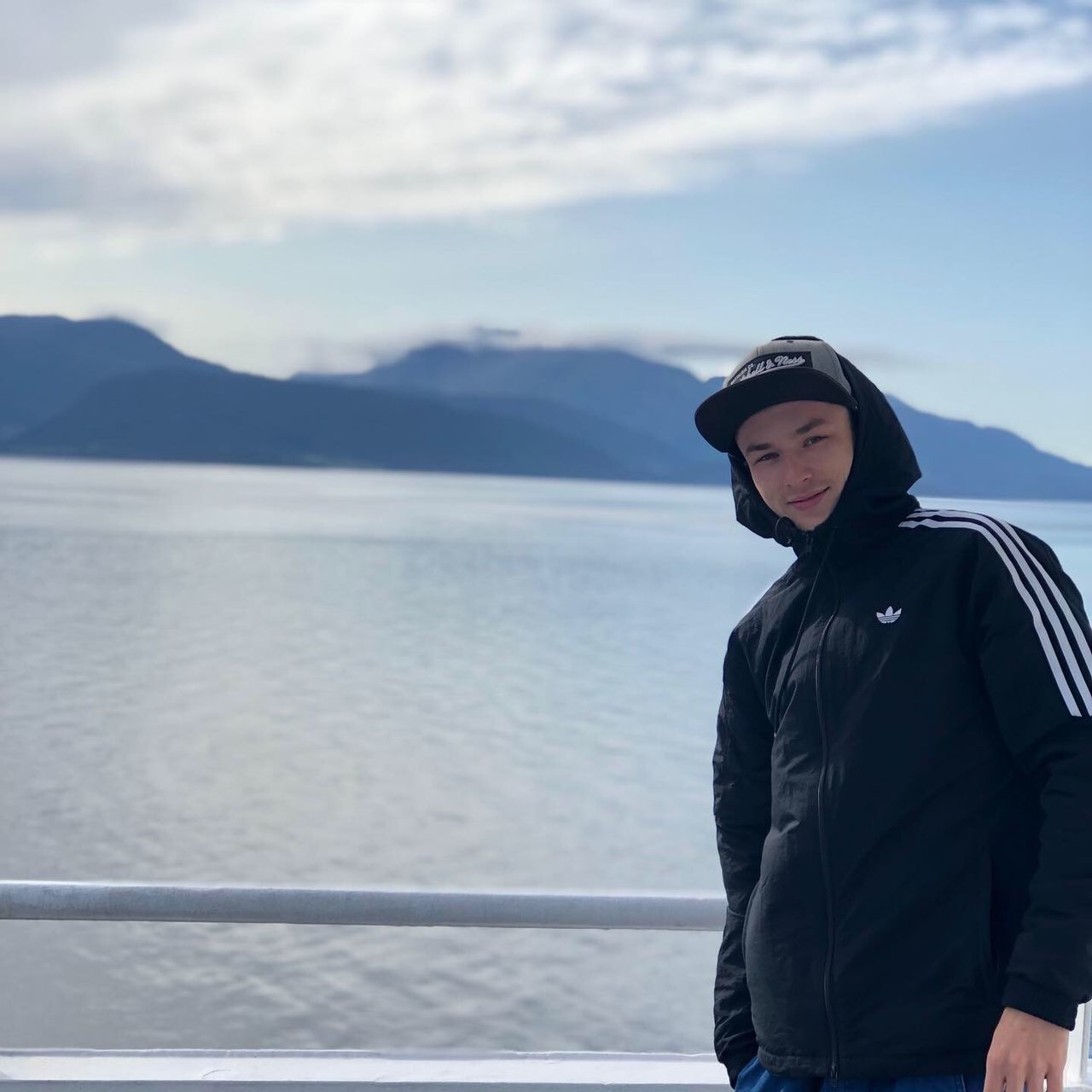 MAN STANDING BY RAILING AGAINST SEA