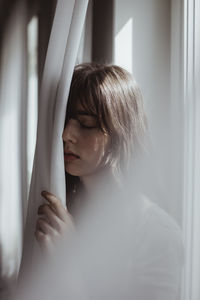 Worried woman standing by curtain