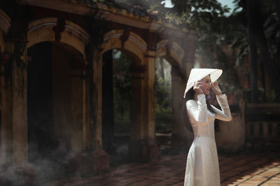 Woman holding umbrella standing outside temple against building