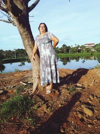 Full length of overweight woman standing by lake against sky