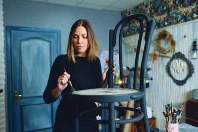 Portrait of young woman painting chair at home