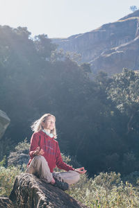 Young woman sitting on mountain against sky