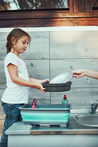 Teenager girl washing up the dishes pots and plates with help her younger sister