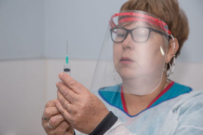 Close-up of doctor wearing face shield holding syringe