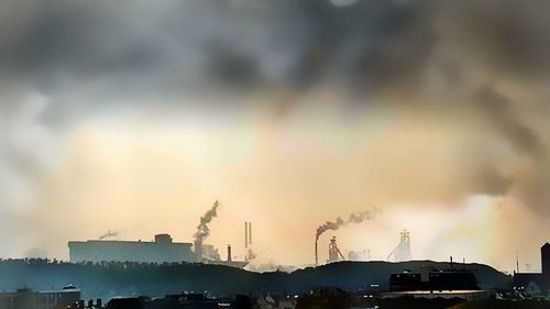 Smoke emitting from factory against cloudy sky