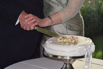 Midsection of couple cutting cake on table