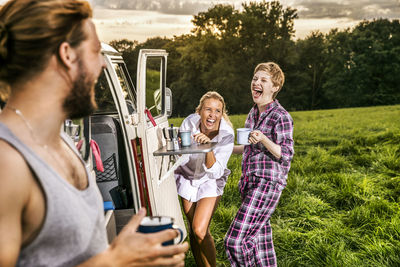 Carefree friends enjoying coffee at a van in rural landscape