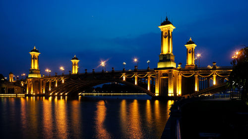 Illuminated bridge over river against buildings at night