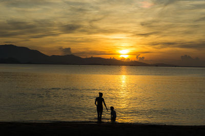 Silhouette people standing on shore against orange sunset sky