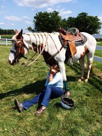 Woman sitting below horse on field