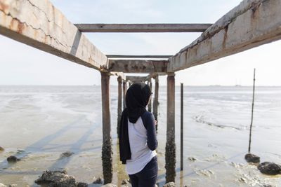 Rear view of woman standing below broken pier at beach