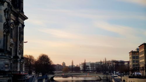 Cars on road by buildings against sky during sunset