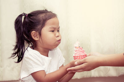 Girl blowing birthday candle on cupcake against curtain
