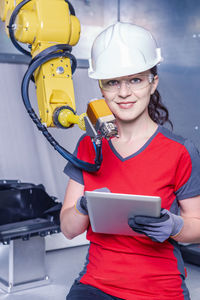 Portrait of smiling technician holding digital tablet while standing by machinery in factory