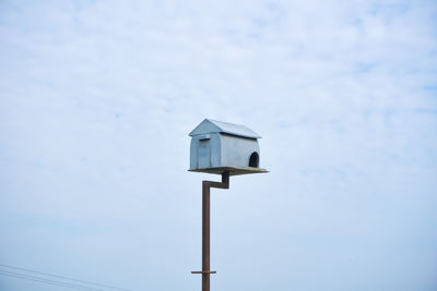 Low angle view of birdhouse on wooden post against sky