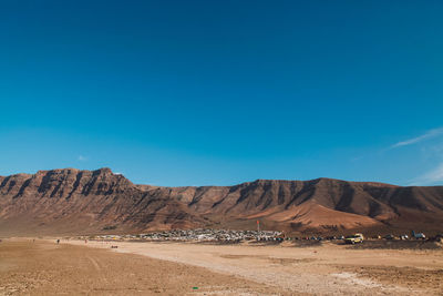 Scenic view of arid landscape and mountains against blue sky