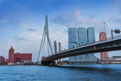 Suspension bridge over river in city against sky