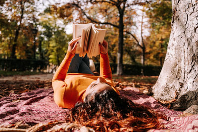 Woman reading book while lying at park during autumn