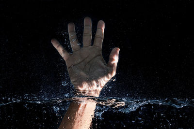 Close-up of hand touching water against black background