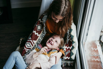 Playful girl laughing while lying on sister lap at home