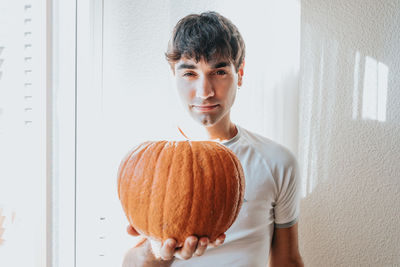 Portrait of man holding pumpkin against wall