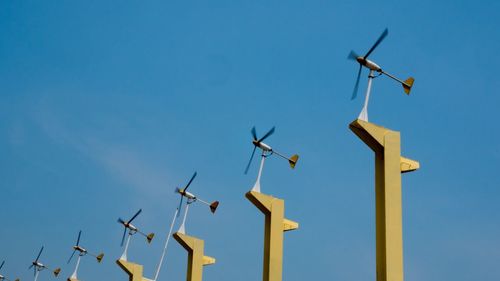 Low angle view of wind turbines against blue sky