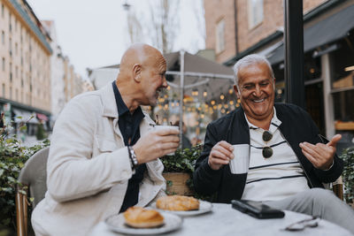 Happy male senior friends enjoying with each other while having coffee at sidewalk cafe