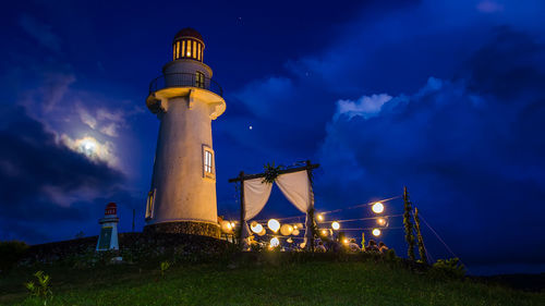 Low angle view of lighthouse by party decoration on hill against blue sky at night