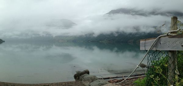Scenic view of lake by mountain during foggy weather