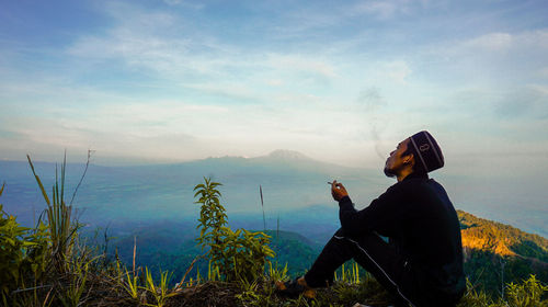 Man sitting on mountain against sky