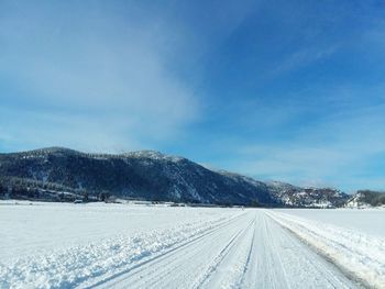 Snow covered road by mountain against sky