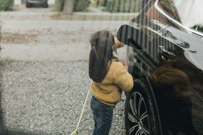 Girl with electric car at charging station seen through glass