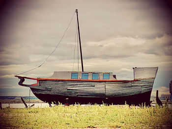 Boat moored on field by sea against sky