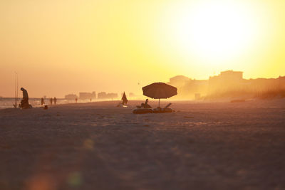 People at beach against clear sky during sunset