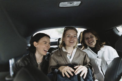 Happy female tourists sitting on back seat in car during road trip