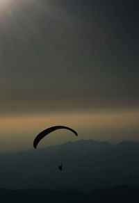 Silhouette person paragliding against sky during sunset