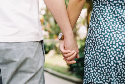 Midsection of couple holding hands while standing outdoors