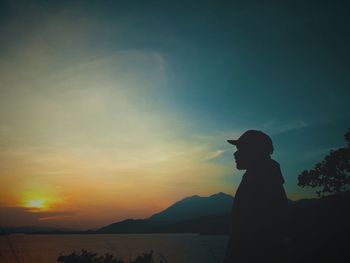 Silhouette man standing by sea against sky during sunset